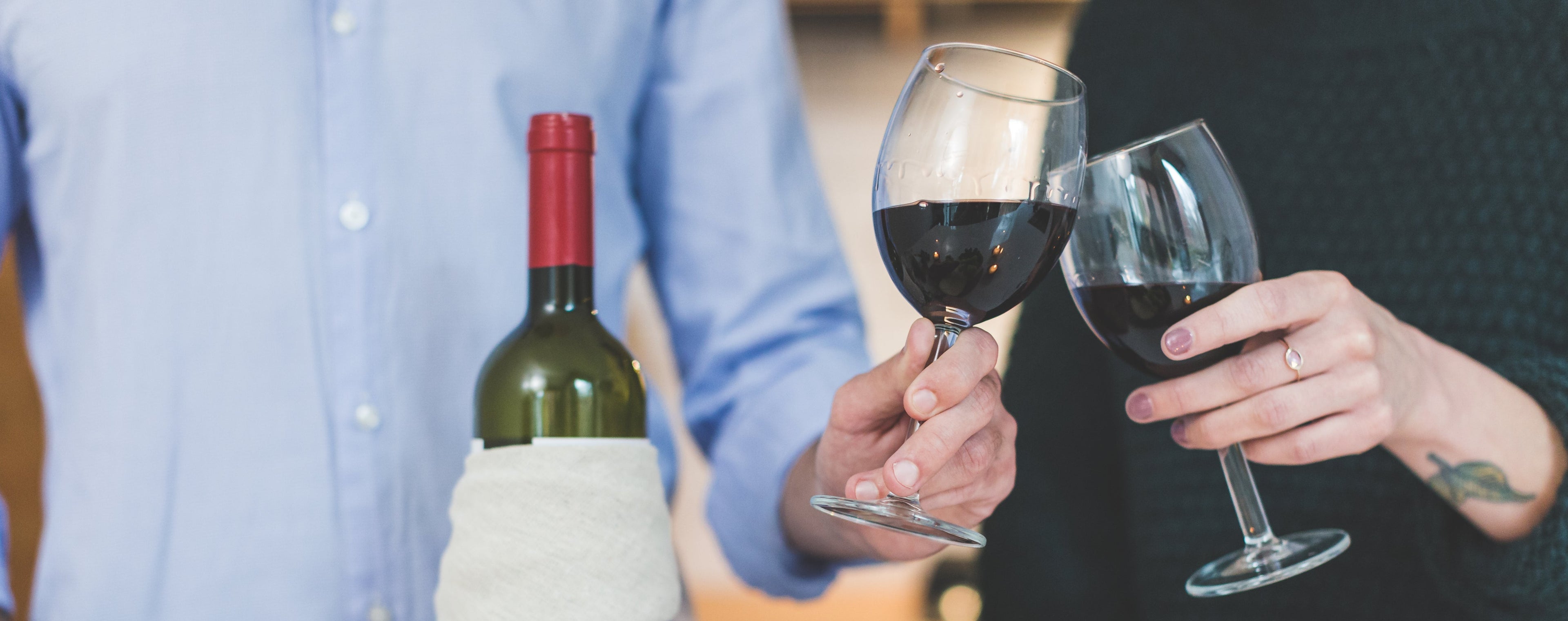 Two people holding wine glasses with a bottle of wine and a table with food and candles in the background.